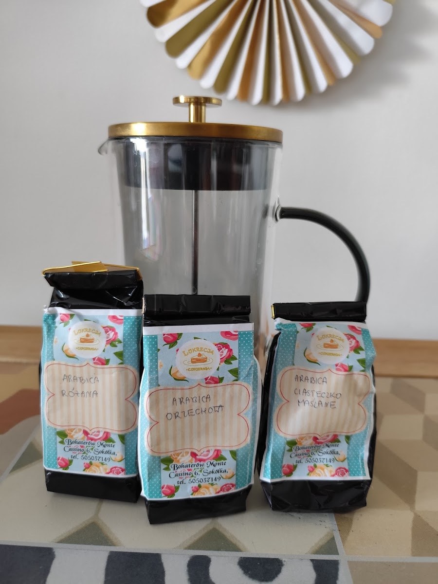 Paczki kawy z etykietami Lukrecji ustawione przy dzbanku z zaparzaczem